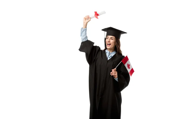 Estudante do sexo feminino em vestido acadêmico torcendo e segurando bandeira canadense com diploma isolado em branco — Fotografia de Stock