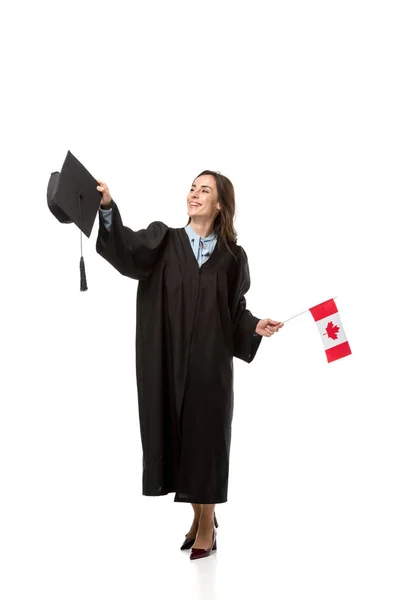 Estudiante en bata académica sosteniendo bandera canadiense y mortero aislado en blanco - foto de stock