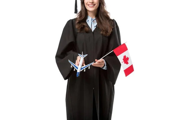 Cropped view of female student in academic gown holding canadian flag and plane model isolated on white, studying abroad concept — Stock Photo