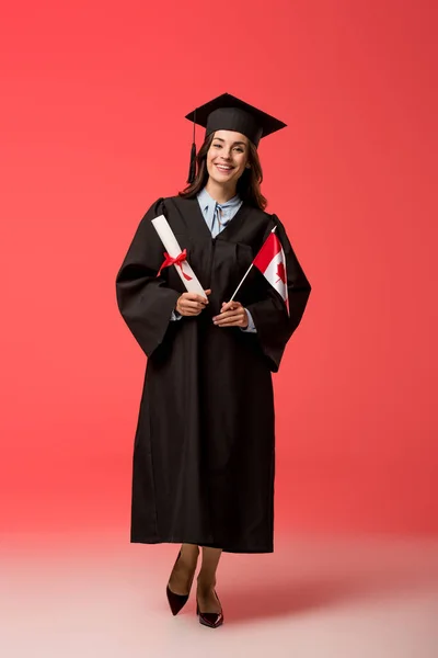 Studente donna in abito accademico con bandiera canadese e diploma su sfondo corallo vivente — Foto stock