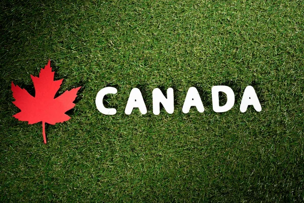 Word 'Canada' with maple leaf on green grass background — Stock Photo