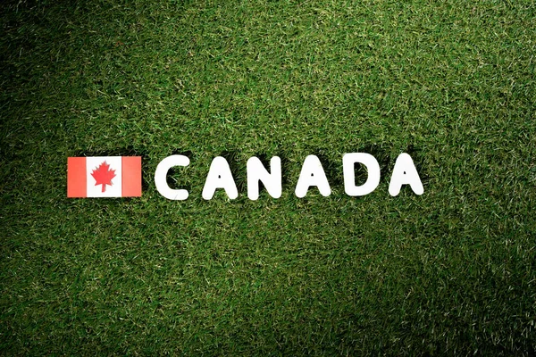 Top view of word 'Canada' with canadian flag on green grass background — Stock Photo