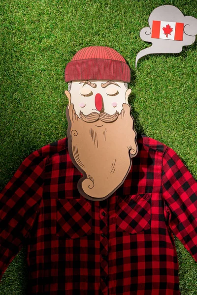 Cardboard man in plaid shirt and thought bubble with canadian flag on green grass background — Stock Photo