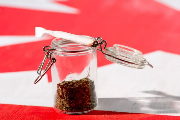 Cannabis in glass jar with joint on canadian flag, marijuana legalization concept — Stock Photo