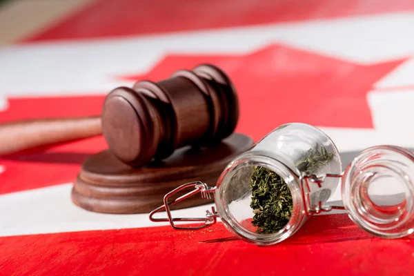 Selective focus of cannabis in glass jar with wooden gavel on canadian flag, marijuana legalization concept — Stock Photo