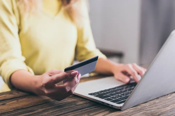 Vista cortada de mulher segurando cartão de crédito perto de laptop em casa — Fotografia de Stock