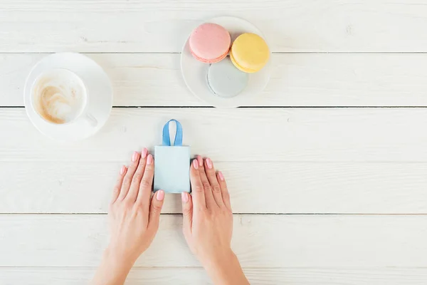 Vista superior da mulher segurando pequeno saco de compras perto de macaroons e café — Fotografia de Stock