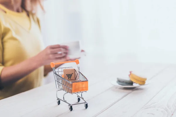 Selective focus of small paper boxes in toy shopping trolley with woman on background — Stock Photo