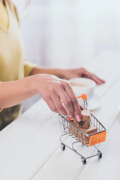 Mise au point sélective de la femme mettant la boîte en papier jouet dans un petit chariot avec tasse sur fond — Photo de stock