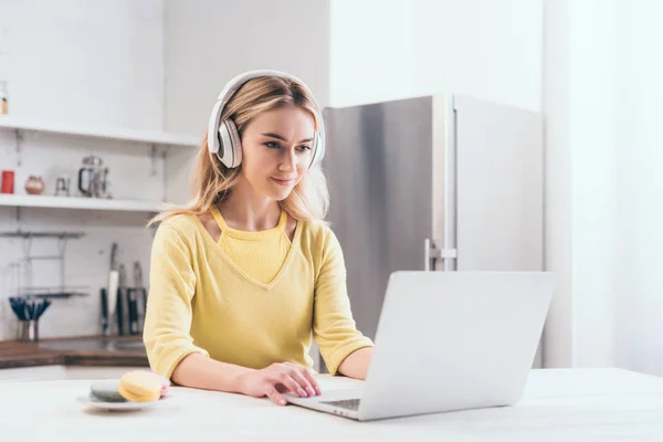 Mulher loira atraente ouvir música em fones de ouvido enquanto usa laptop — Fotografia de Stock