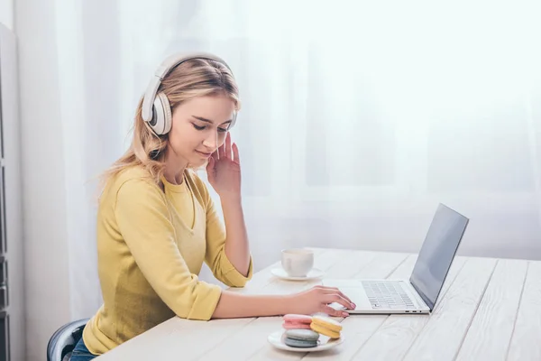 Blonde woman listening music in headphones while looking at macaroons — Stock Photo