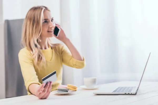 Enfoque selectivo de la tarjeta de crédito en la mano de la atractiva mujer rubia hablando en el teléfono inteligente - foto de stock