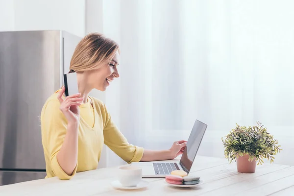 Cheerful woman holding credit card while looking at laptop — Stock Photo