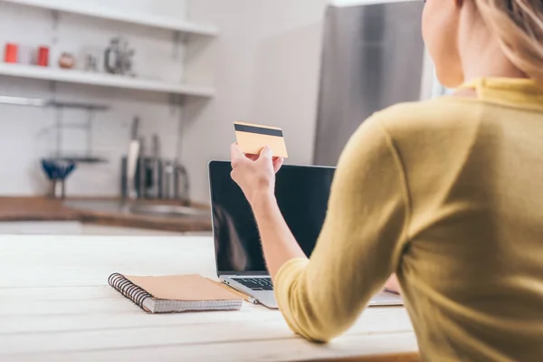 Vue recadrée de la femme tenant la carte de crédit près d'un ordinateur portable à la maison — Photo de stock