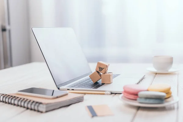 Selective focus of small paper boxes on laptop near macaroons and smartphone on notebook — Stock Photo