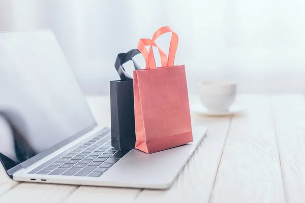 Foco seletivo de pequenos sacos de compras no laptop com copo no fundo — Fotografia de Stock