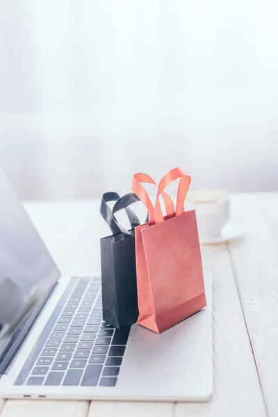 Foco selectivo de pequeñas bolsas de compras en el teclado del ordenador portátil con taza de café en el fondo - foto de stock