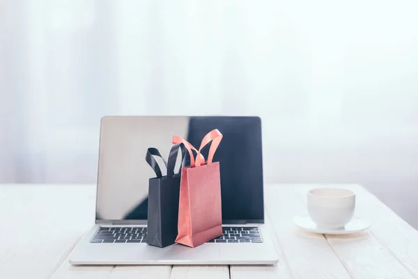 Kleine Einkaufstaschen auf Laptop-Tastatur mit Tasse auf Hintergrund — Stockfoto