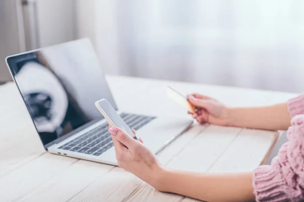 Agrafé ciew de femme tenant carte de crédit et smartphone près d'un ordinateur portable — Photo de stock