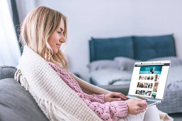Attraktive blonde Frau benutzt Laptop mit Amazon-Website auf dem Bildschirm und hält Kreditkarte — Stockfoto