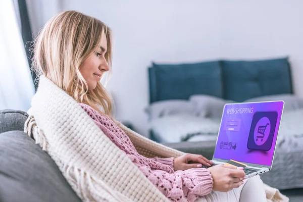 Atractiva mujer rubia usando el ordenador portátil con el sitio web de compras en la pantalla y la celebración de la tarjeta de crédito - foto de stock