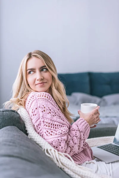 Atractiva mujer sosteniendo taza con bebida en casa - foto de stock