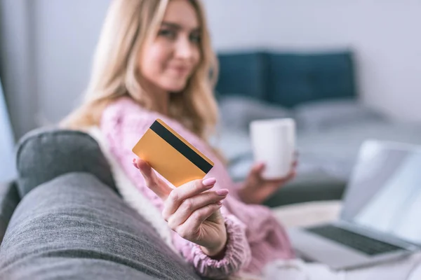 Enfoque selectivo de la tarjeta de crédito en las manos de la mujer rubia sosteniendo taza con bebida - foto de stock