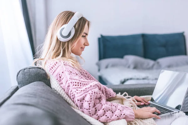 Mulher atraente em fones de ouvido usando laptop em casa — Fotografia de Stock