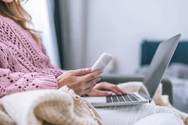 Vista cortada do blogueiro feminino usando laptop e segurando smartphone em casa — Fotografia de Stock