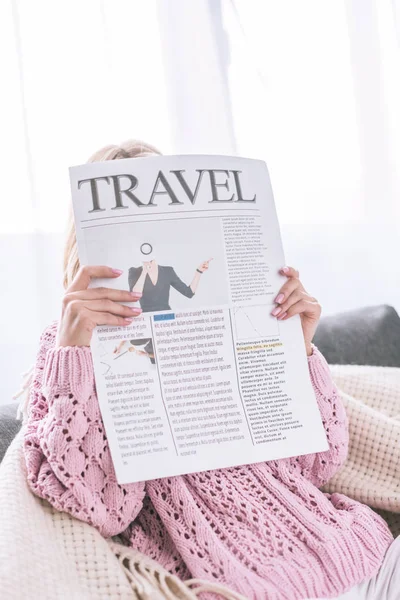 Mujer leyendo el periódico de viaje mientras está sentada en casa - foto de stock