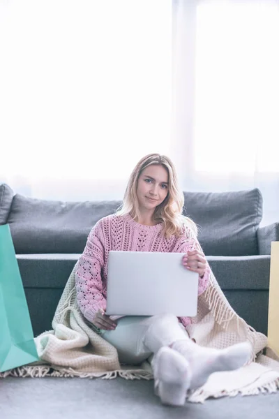 Cheerful blonde woman sitting on floor near sofa with laptop — Stock Photo