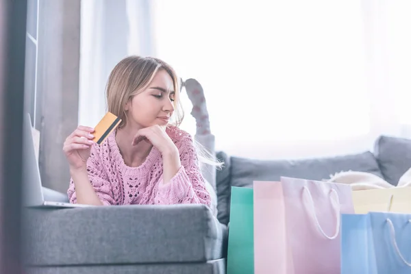 Bella donna in possesso di carta di credito mentre sdraiato sul divano e guardando le borse della spesa — Foto stock