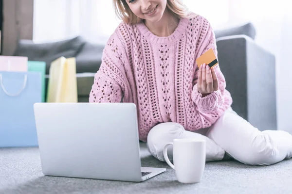 Ausgeschnittene Ansicht einer fröhlichen Frau, die ihre Kreditkarte in der Hand hält und neben ihrem Laptop sitzt — Stockfoto