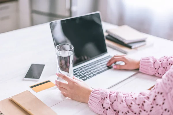 Vista cortada de mulher segurando vidro de água perto de laptop na mesa de madeira — Fotografia de Stock