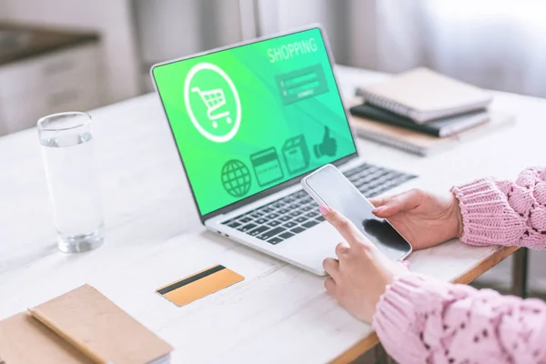 Cropped view of woman holding smartphone near laptop with shopping website on screen — Stock Photo