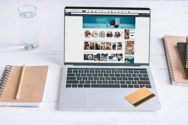 Laptop with Amazon website on screen and credit card on wooden desk — Stock Photo