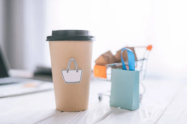 Селективный фокус бумажной чашки с символом рядом с декоративной упаковкой и корзиной с коробками — стоковое фото