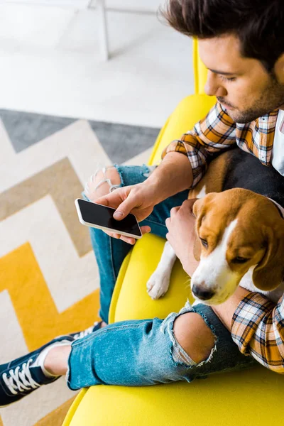 Bel homme utilisant smartphone assis sur le canapé avec chien — Photo de stock