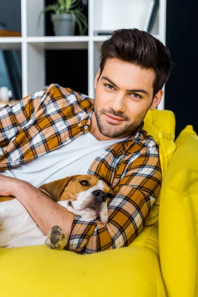 Handsome smiling man relaxing on sofa with beagle dog — Stock Photo