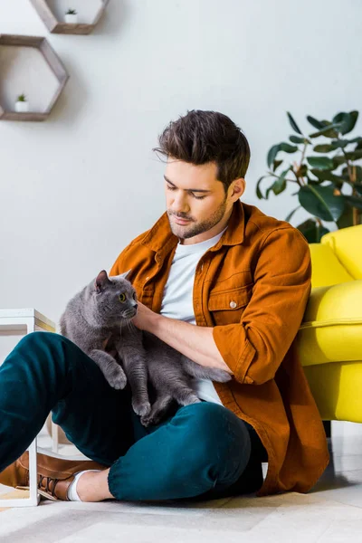 Casual smiling man sitting on floor with cute cat — Stock Photo