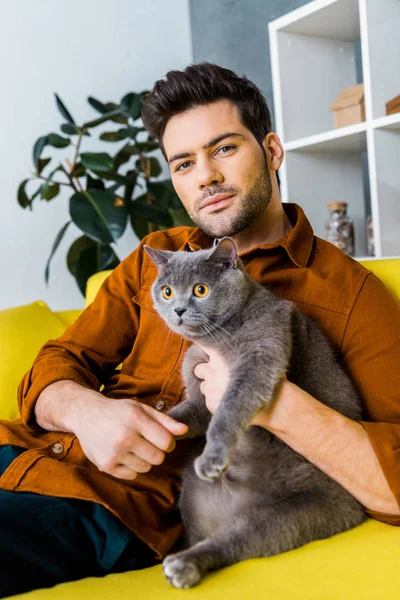 Schöner Mann mit süßer Katze sitzt zu Hause auf dem Sofa — Stockfoto