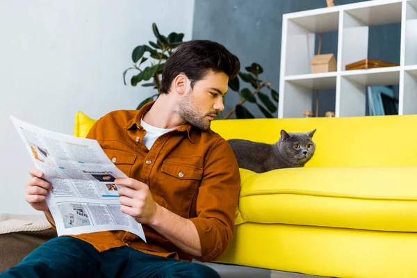 Молодой человек держит газету и смотрит на кота — стоковое фото