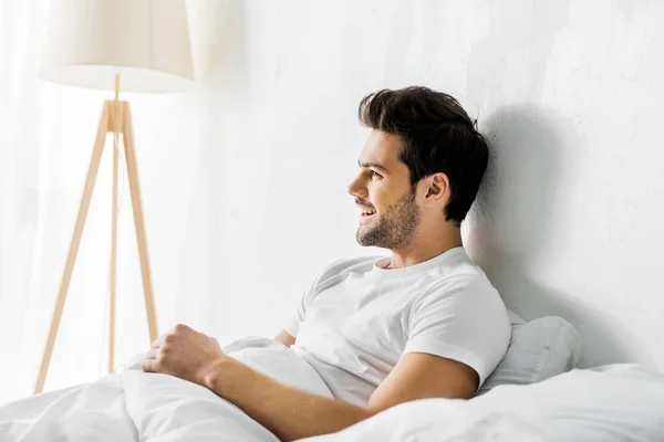Junger lachender Mann liegt morgens im Bett — Stockfoto