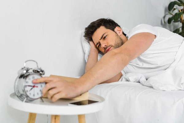 Selective focus of man waking up and taking alarm clock in the morning — Stock Photo
