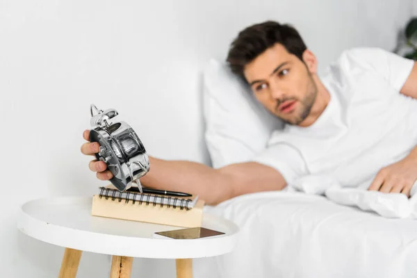 Selective focus of man looking at alarm clock in the morning — Stock Photo