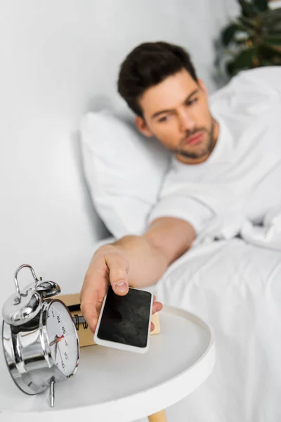 Selective focus of man waking up and taking smartphone in the morning — Stock Photo