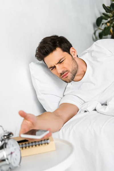Confused man waking up and looking at smartphone in the morning — Stock Photo
