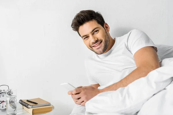 Hombre alegre usando teléfono inteligente en la cama por la mañana - foto de stock
