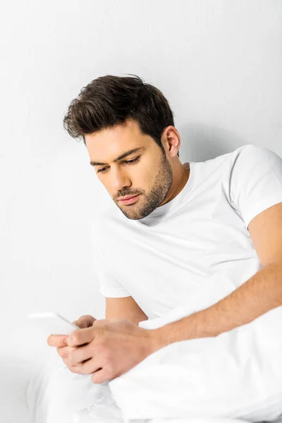 Schöner Mann mit Smartphone, während er morgens im Bett liegt — Stockfoto