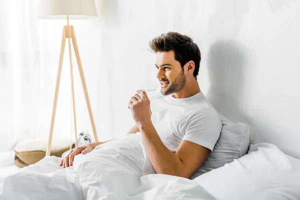 Smiling young man drinking water in bedroom — Stock Photo